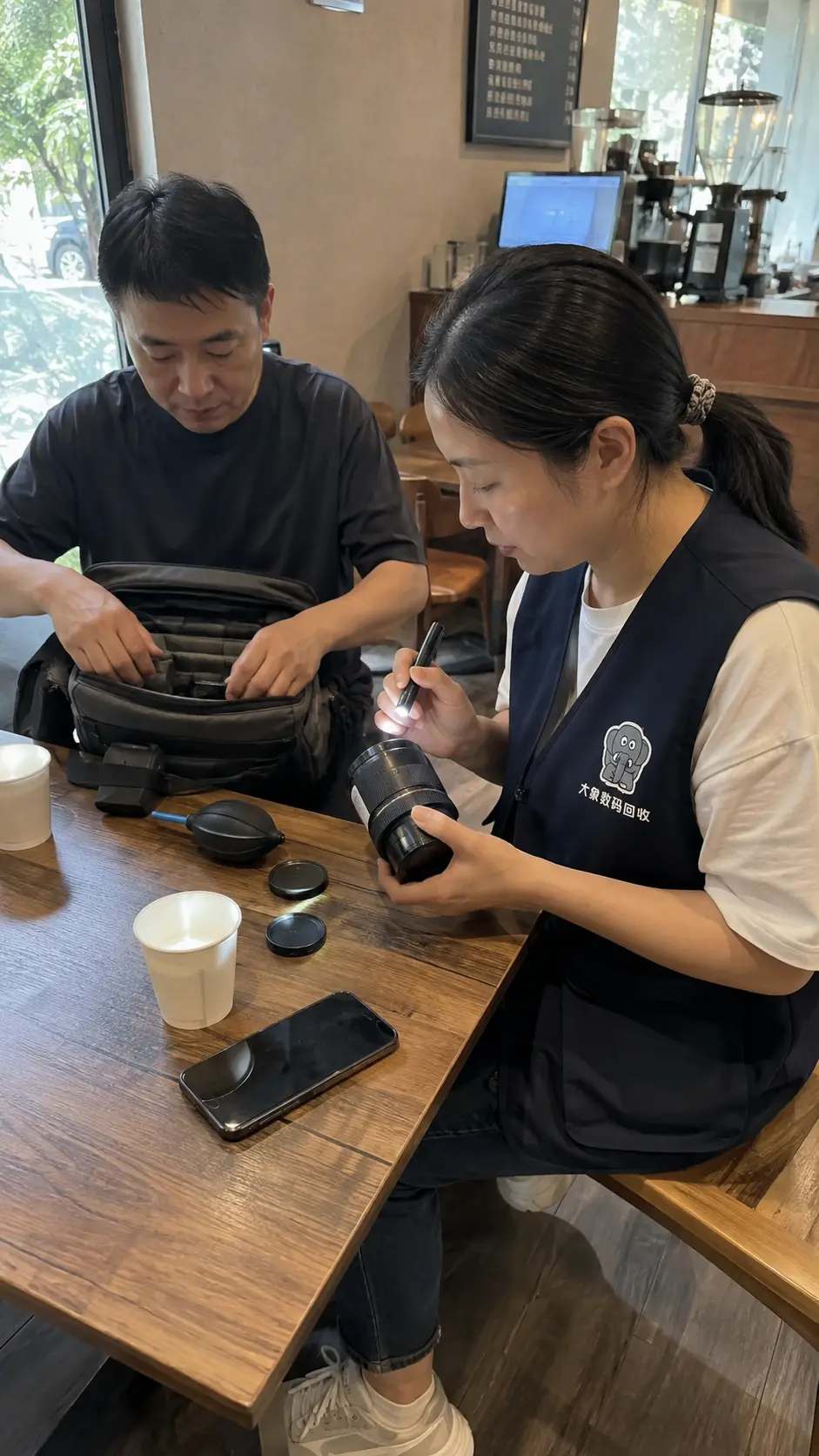 穿着大象数码回收工作马甲的工作人员在咖啡店当面查看镜头状态